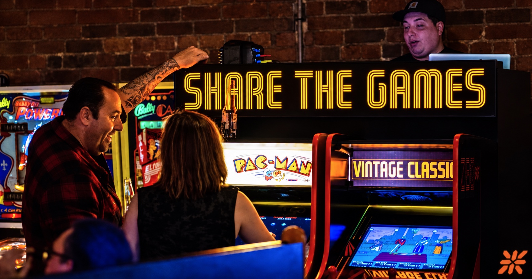 Friends enjoying vintage arcade games beneath ZED*80's Share the Games sign